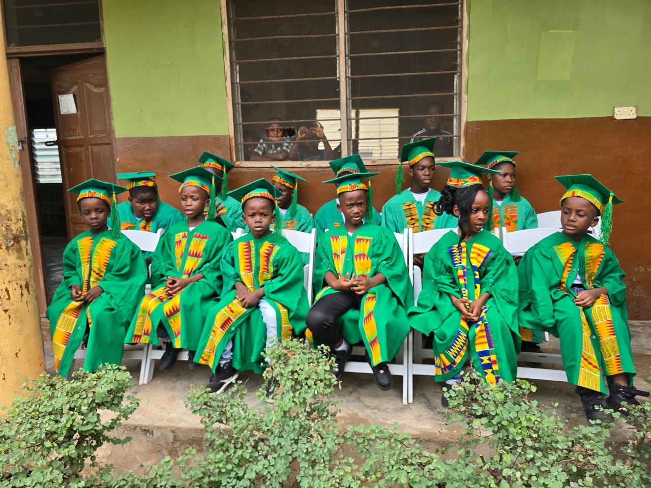 Graduating pupils seated in green gowns and kente stoles